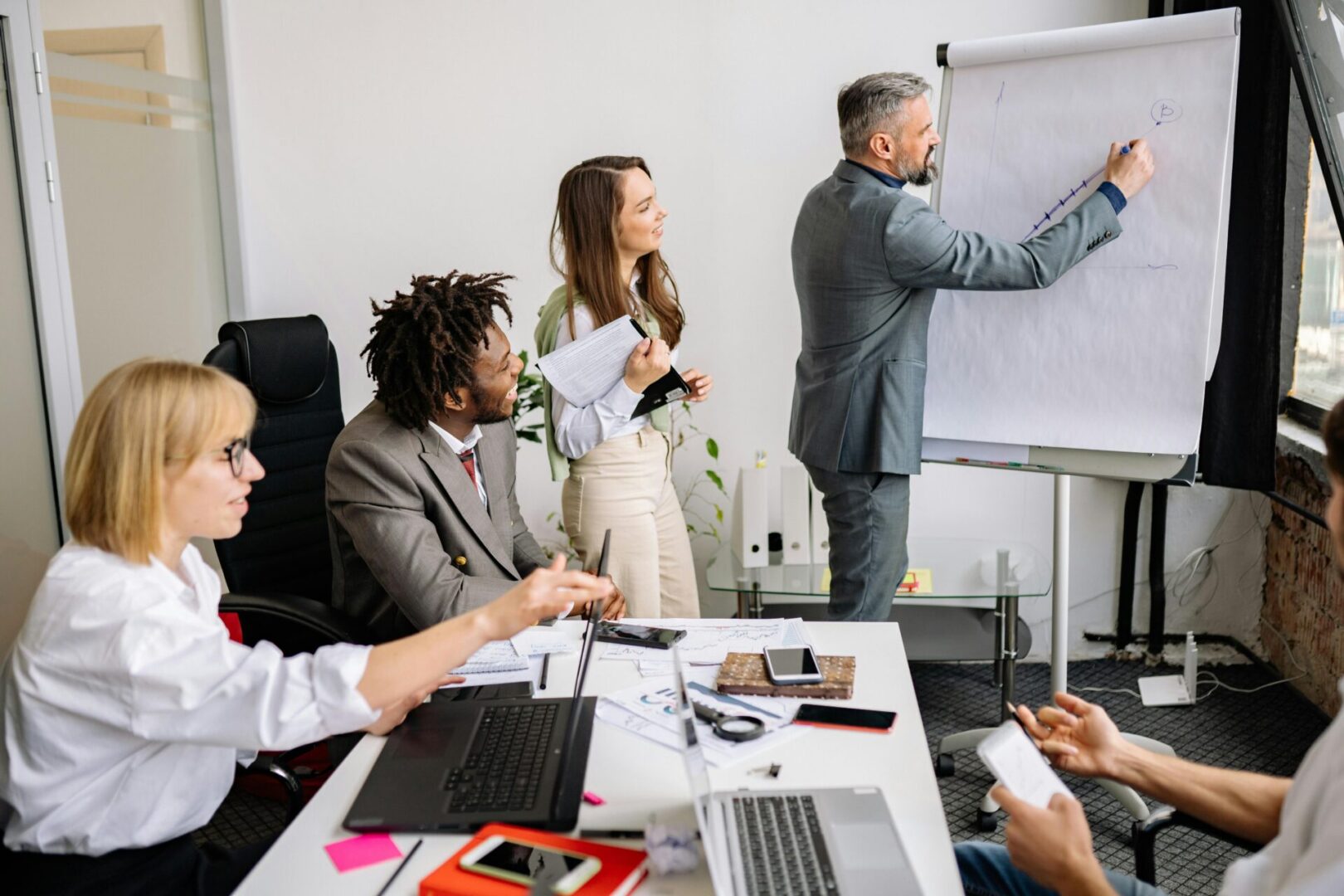 A group of people sitting at tables in front of a whiteboard.